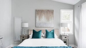Une chambre à coucher comprenant un lit, deux tables de chevet, une fenêtre et une œuvre d’art accrochée au mur.