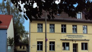 A yellow building with a sign reading "PUMPENFACHHANDEL Norman Zilius Wasseranlagen" and a number "195" on the door. - Cozy vacation apartment near the Müggelsee lake (Berlin)