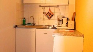 A compact kitchen with white cabinets, a sink, a coffee maker, and a red checkered rug on the floor. - Cozy vacation apartment near the Müggelsee lake (Berlin)