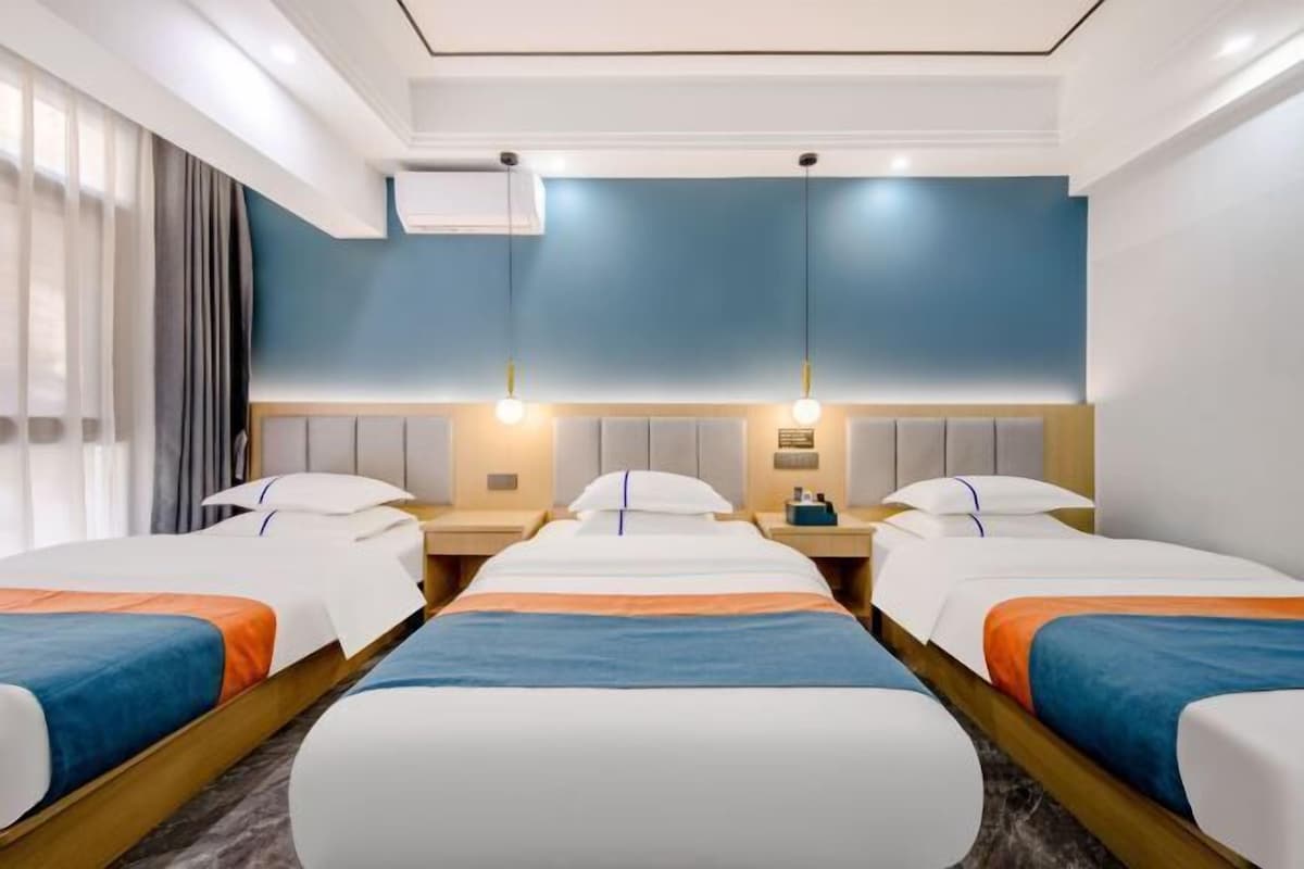 A hotel room with two beds, a nightstand, a wall-mounted air conditioner, and a window with curtains.