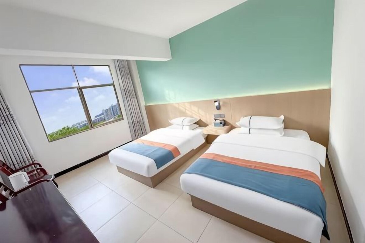 A hotel room with two beds, a desk, and a large window with a city view.