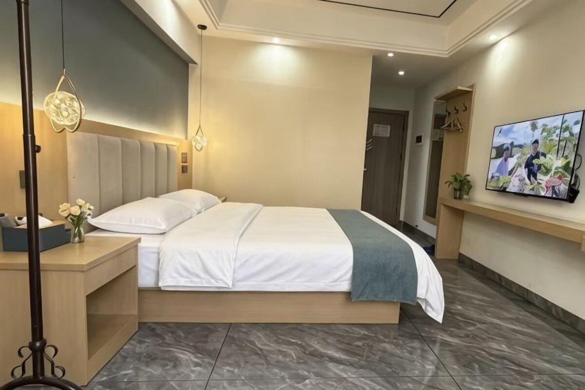 A modern hotel room with a bed, bedside table, lamp, and a flat-screen TV mounted on the wall.