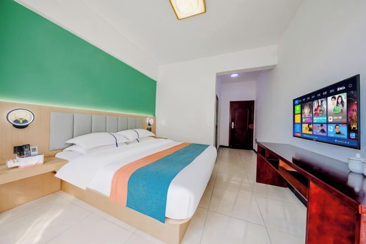 Ein Hotelzimmer mit Bett, Fernseher an der Wand, Schreibtisch und einer grünen Wand.