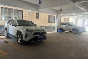 A parking garage with two white SUVs parked inside. - Mingzhu Hotel (Gasa Airport Railway Station) (Jinghong)
