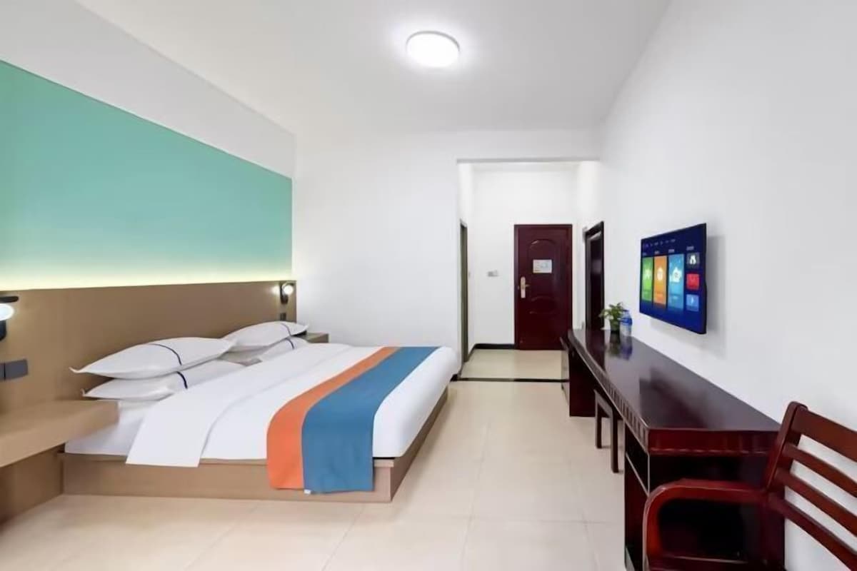 A hotel room with a bed, bedside table, desk, chair, and a TV on the wall.