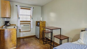 A compact room with a kitchenette, a single bed, and a small table.
