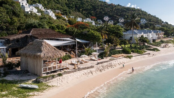 Un complexe hôtelier en bord de mer, avec des bungalows aux toits de chaume, des chaises longues et une vue sur l’océan.