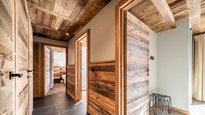 A hallway with wooden panel walls and a tiled floor, leading to an open room with a bed and a window.