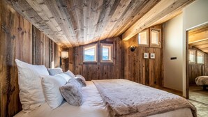 A cozy bedroom with a wooden ceiling, a large bed with white linens, and two windows providing natural light.