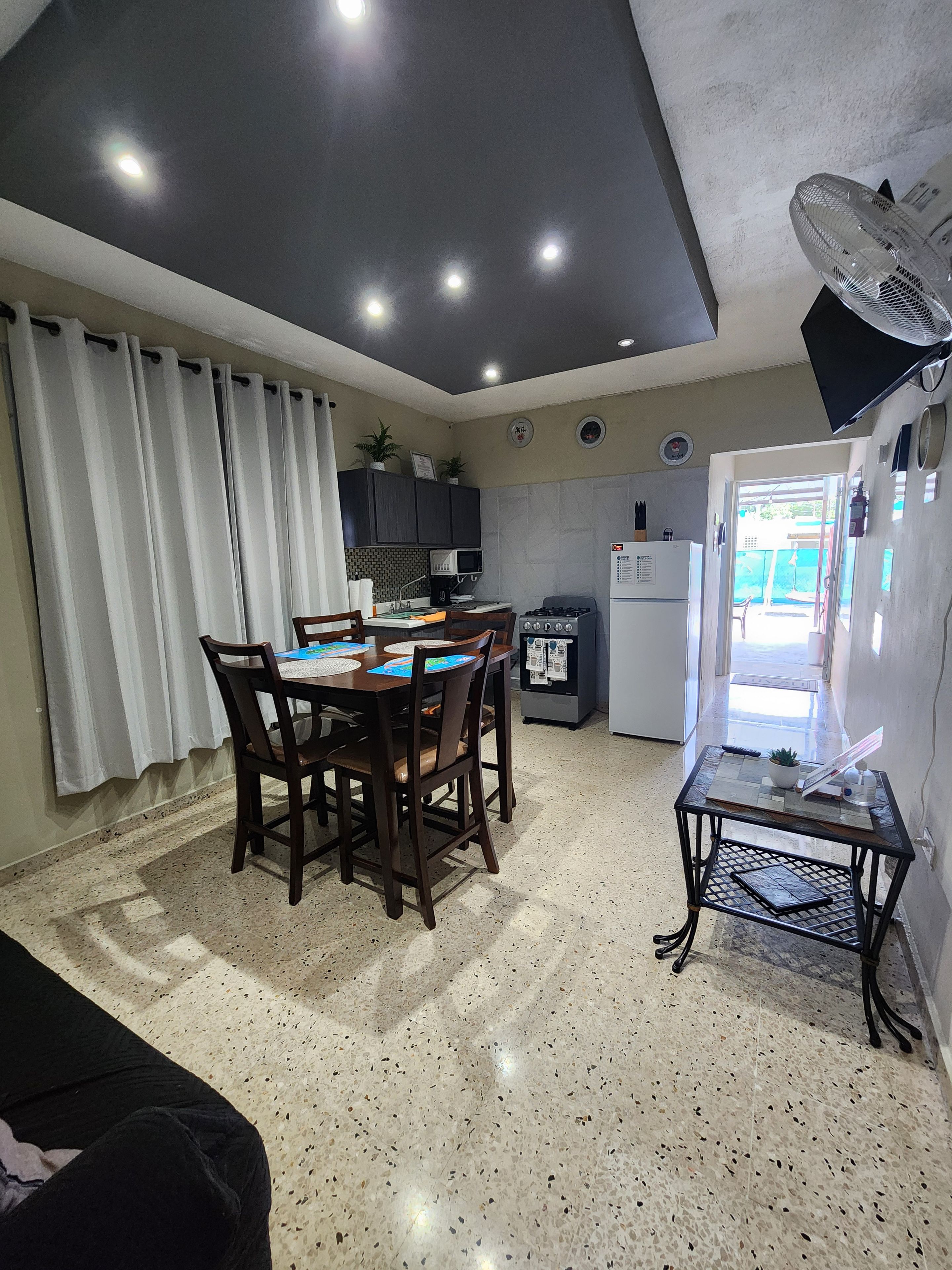 A compact living space with a dining area, kitchenette, and a small table with a fan.