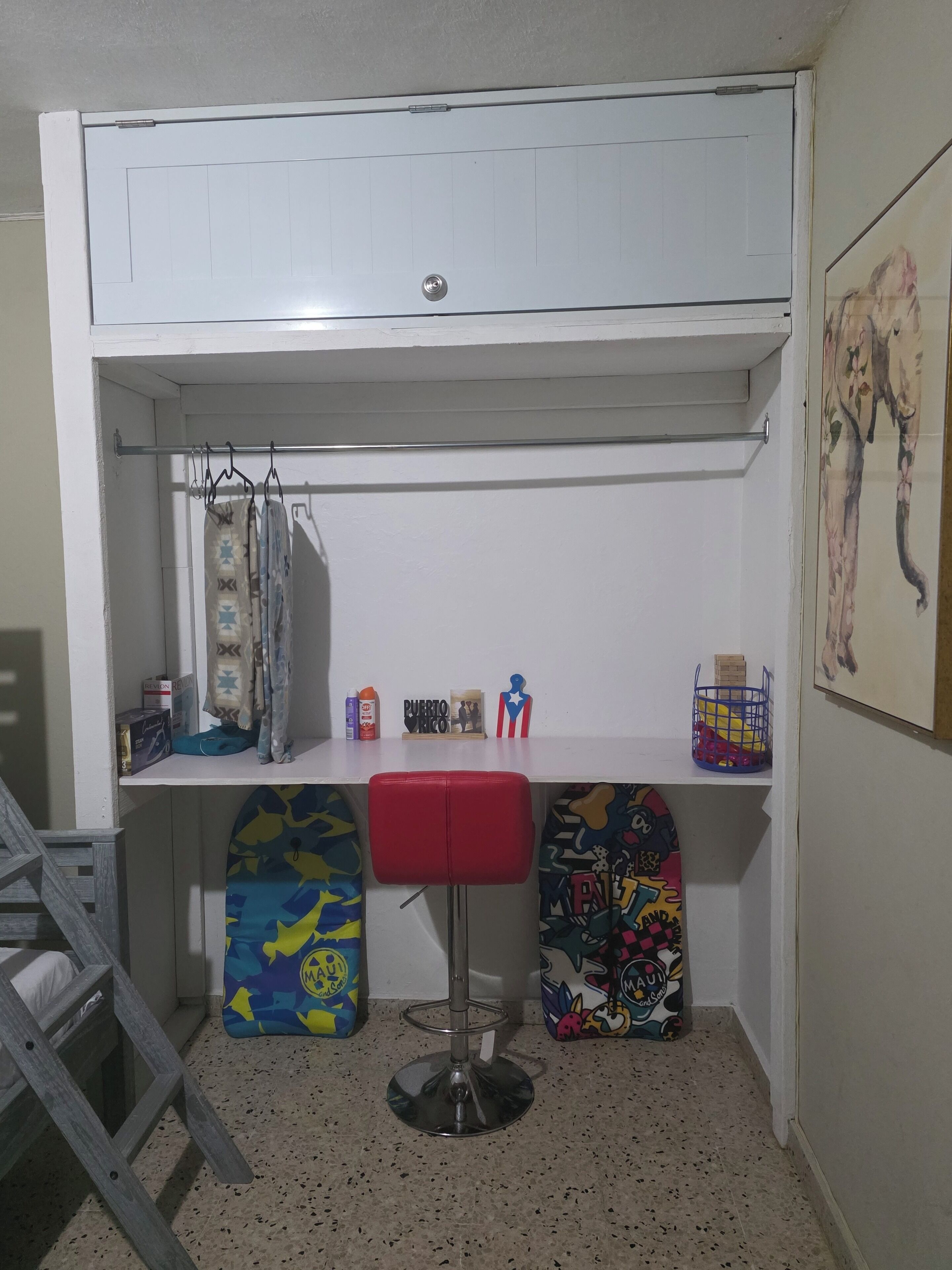 Een kleine kamer met een stapelbed, een bureau met stoel, een plank met diverse spullen, en een trap.