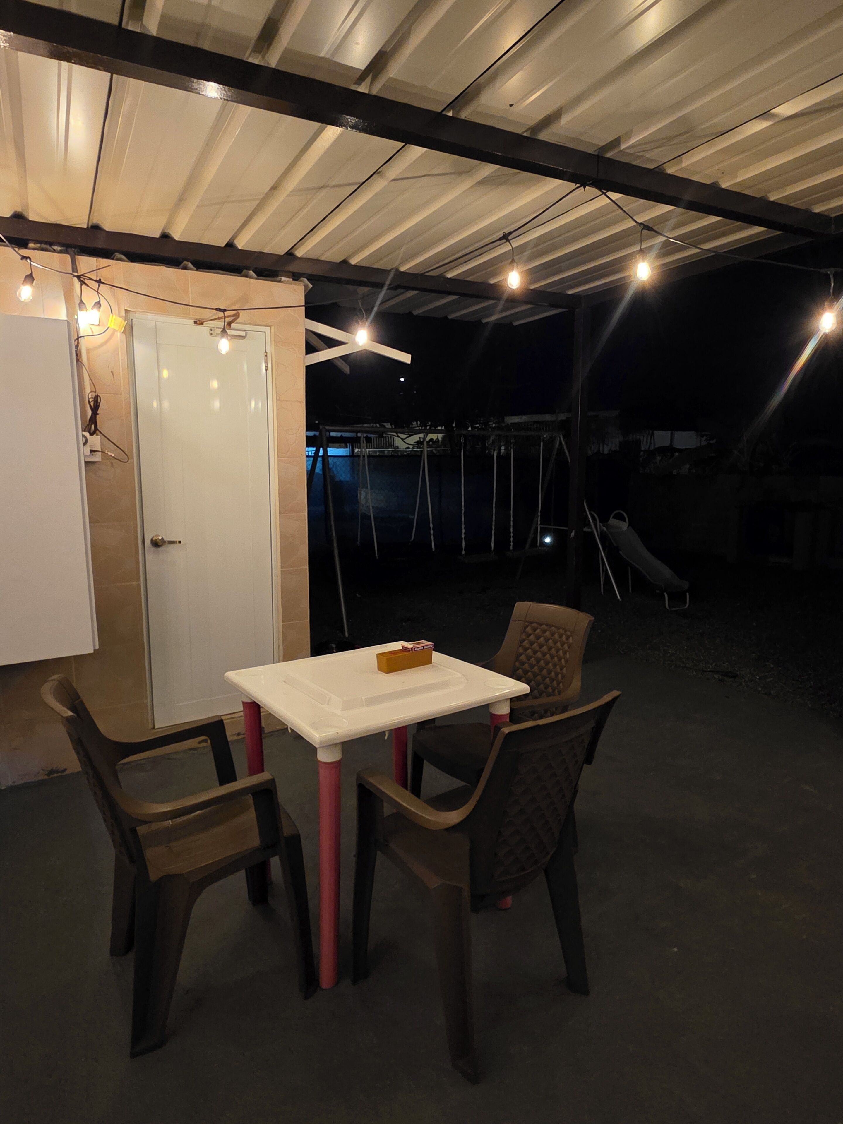 An outdoor patio with a table and chairs, a swing set, and a door.