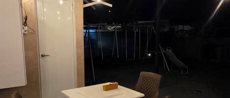 An outdoor patio with a table and chairs, a swing set, and a door.