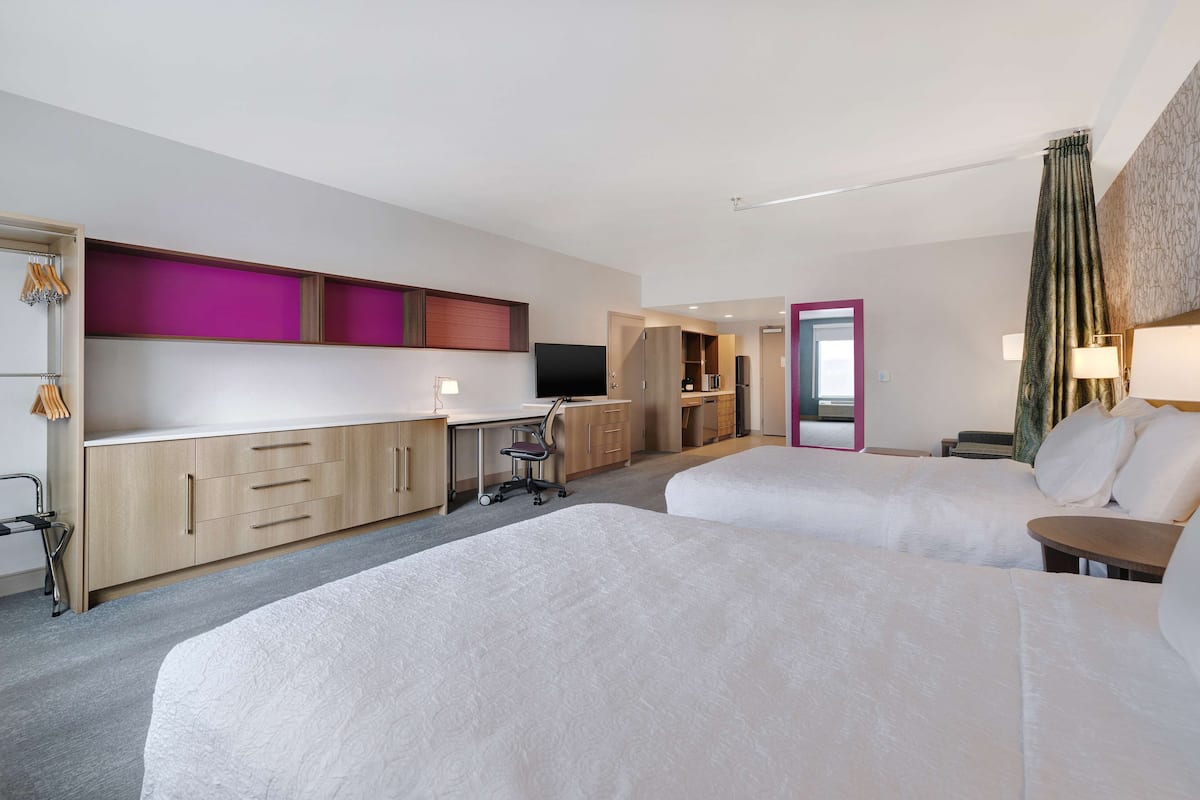 Ett hotellrum med två sängar, ett skrivbord, en stol, en TV och en garderob.