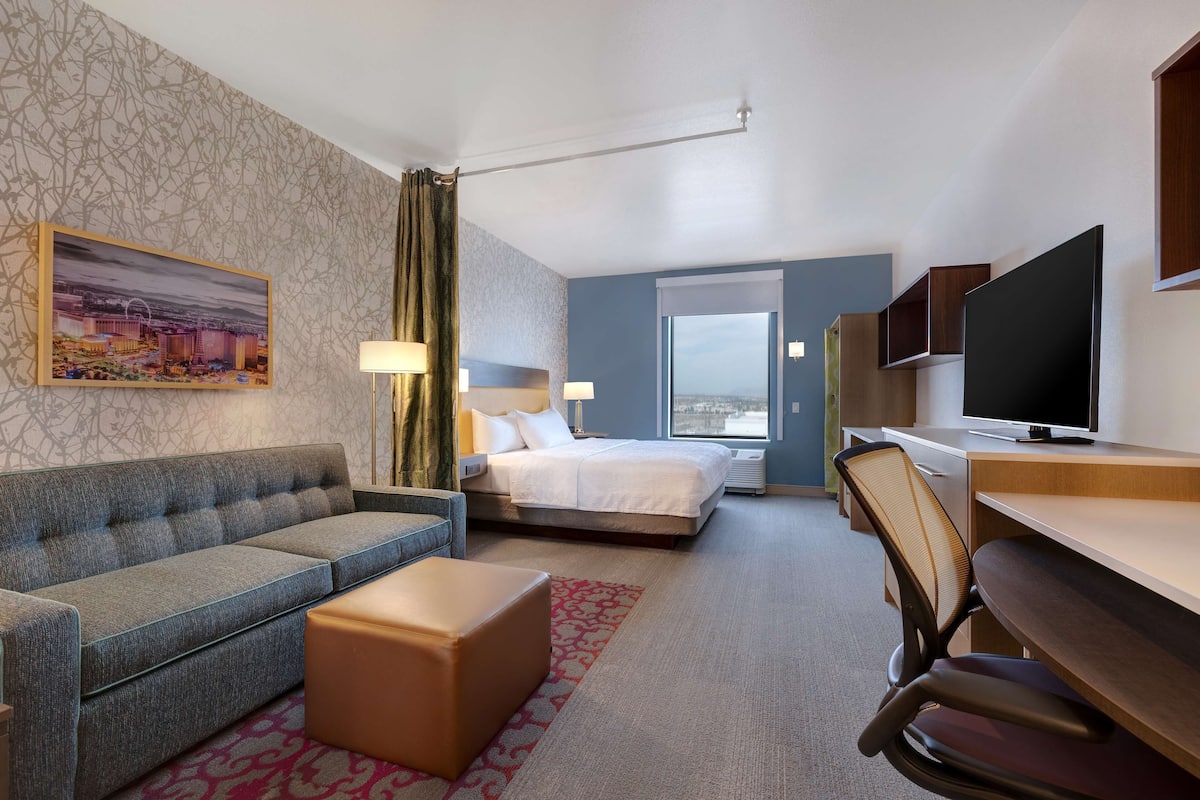 Ett hotellrum med en soffa, en säng, ett skrivbord, en tv och ett fönster med utsikt över staden.