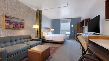 Ein Hotelzimmer mit einer Couch, einem Bett, einem Schreibtisch, einem Fernseher und einem Fenster mit Blick auf die Stadt.