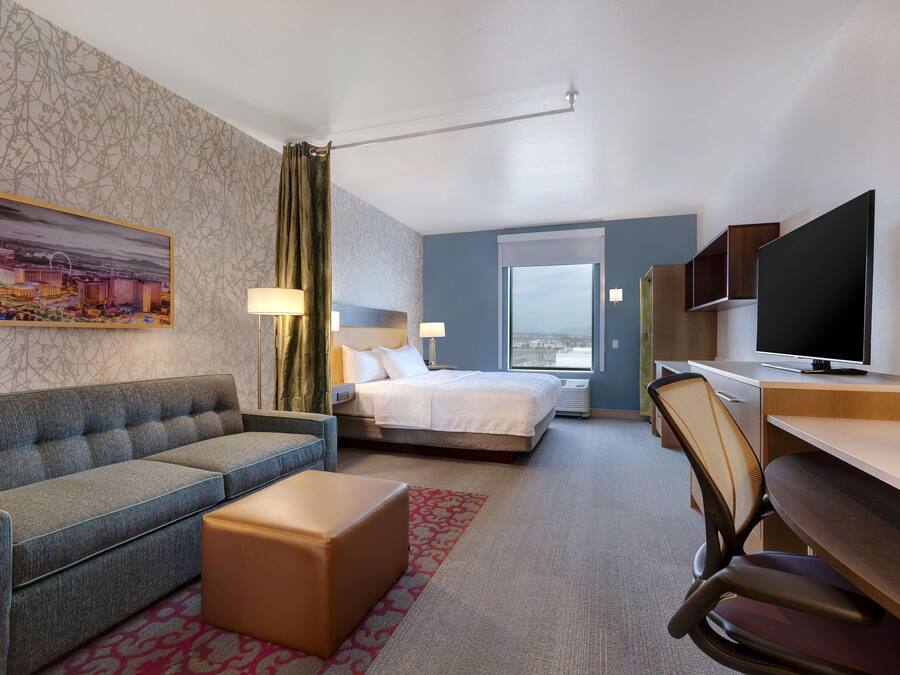 Ein Hotelzimmer mit einer Couch, einem Bett, einem Schreibtisch, einem Fernseher und einem Fenster mit Blick auf die Stadt.
