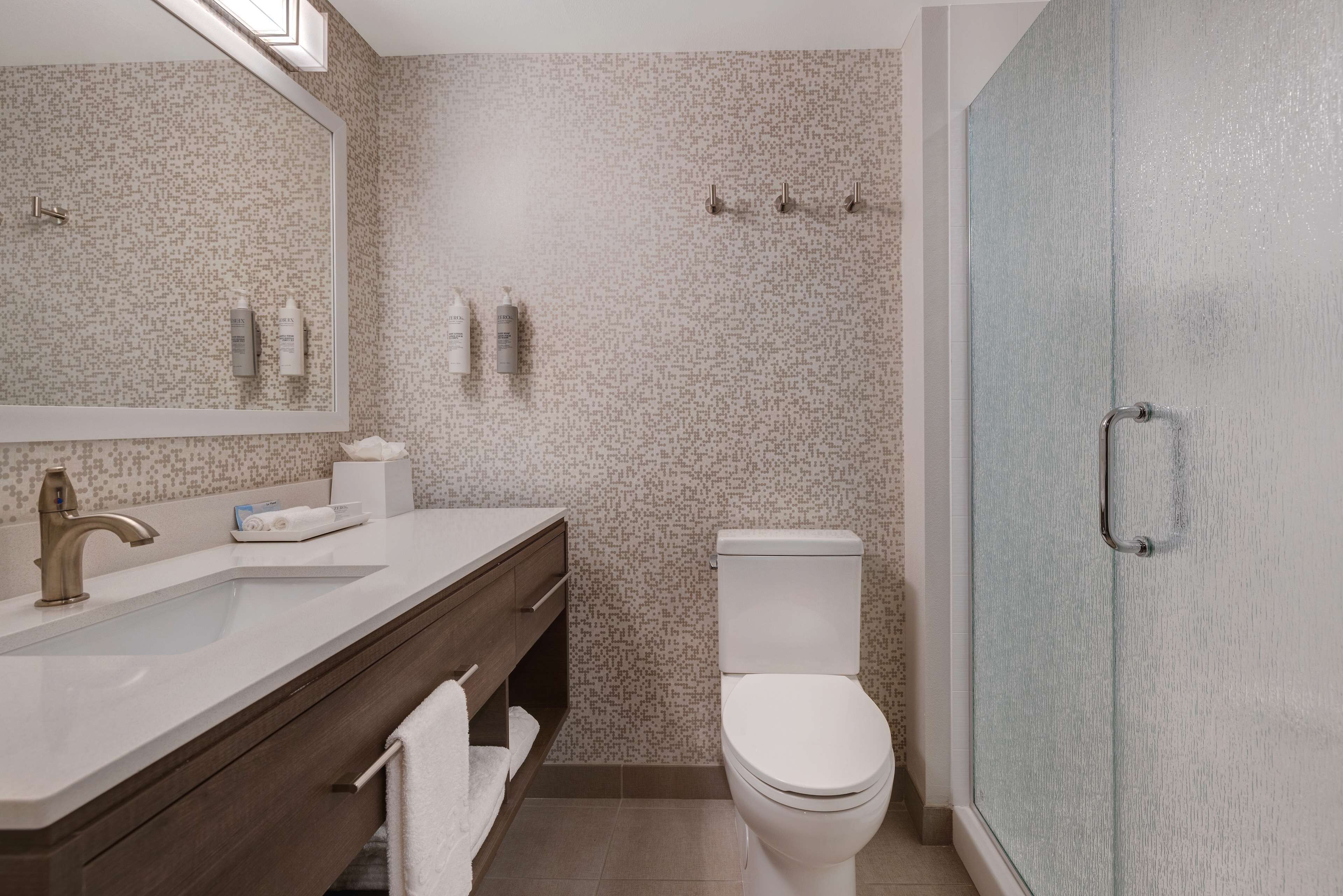 A modern bathroom with a large mirror, a sink, a toilet, and a glass shower enclosure.