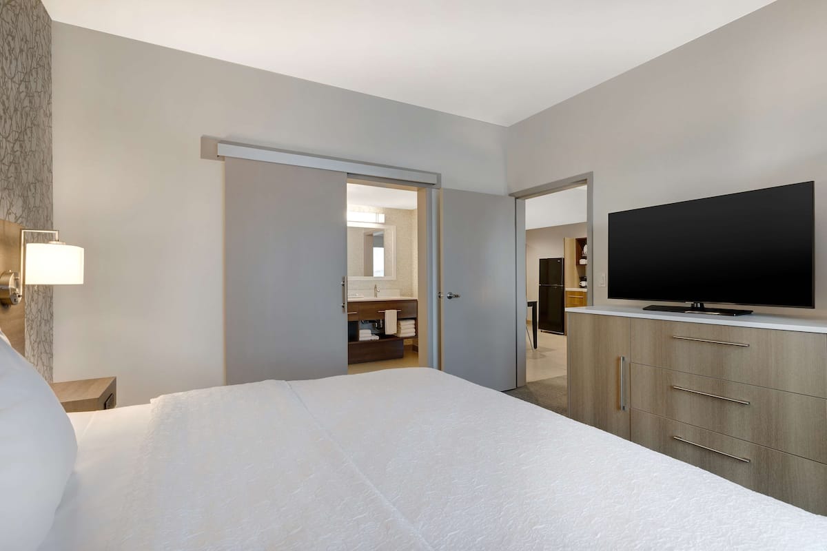 Ett hotellrum med en stor säng, en platt-TV, en garderob och ett badrum som syns genom en öppen dörr.