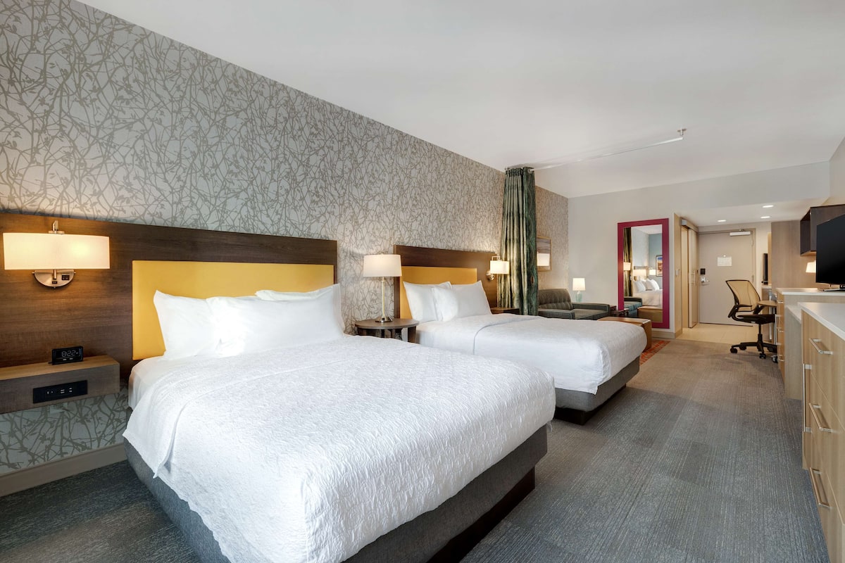 Ett hotellrum med två sängar, ett skrivbord, en stol och en TV.