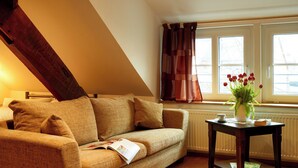 A cozy room with a sloped ceiling, a sofa, a table with a vase of flowers, and a window with curtains. - **** Holiday home 'old farmhouse' (Burgen)