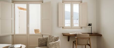 A room with two open doors, a desk with a chair, a small table with a book, and a lamp.
