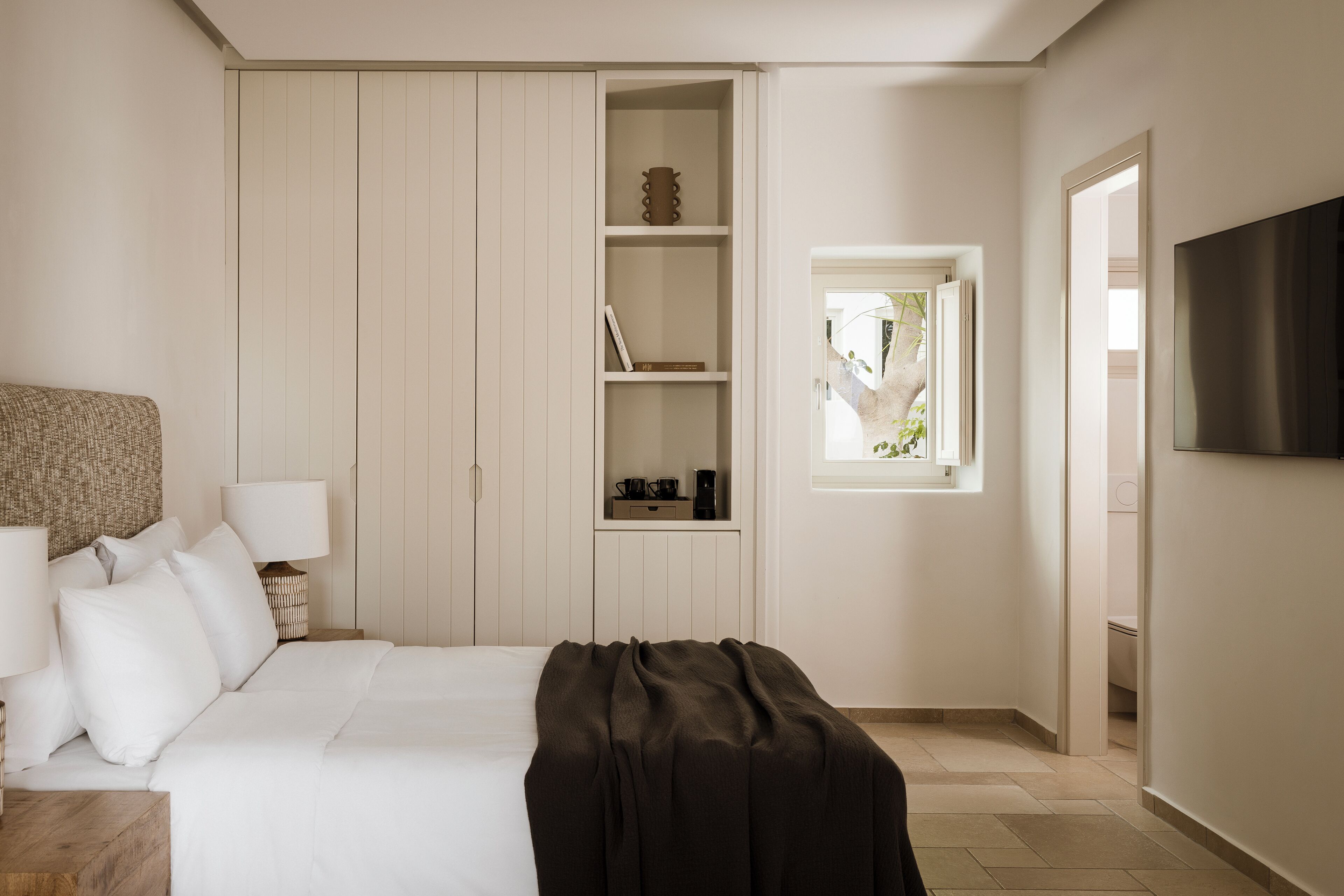 Un dormitorio con cama, lámparas de noche, armario, estantería y televisor.