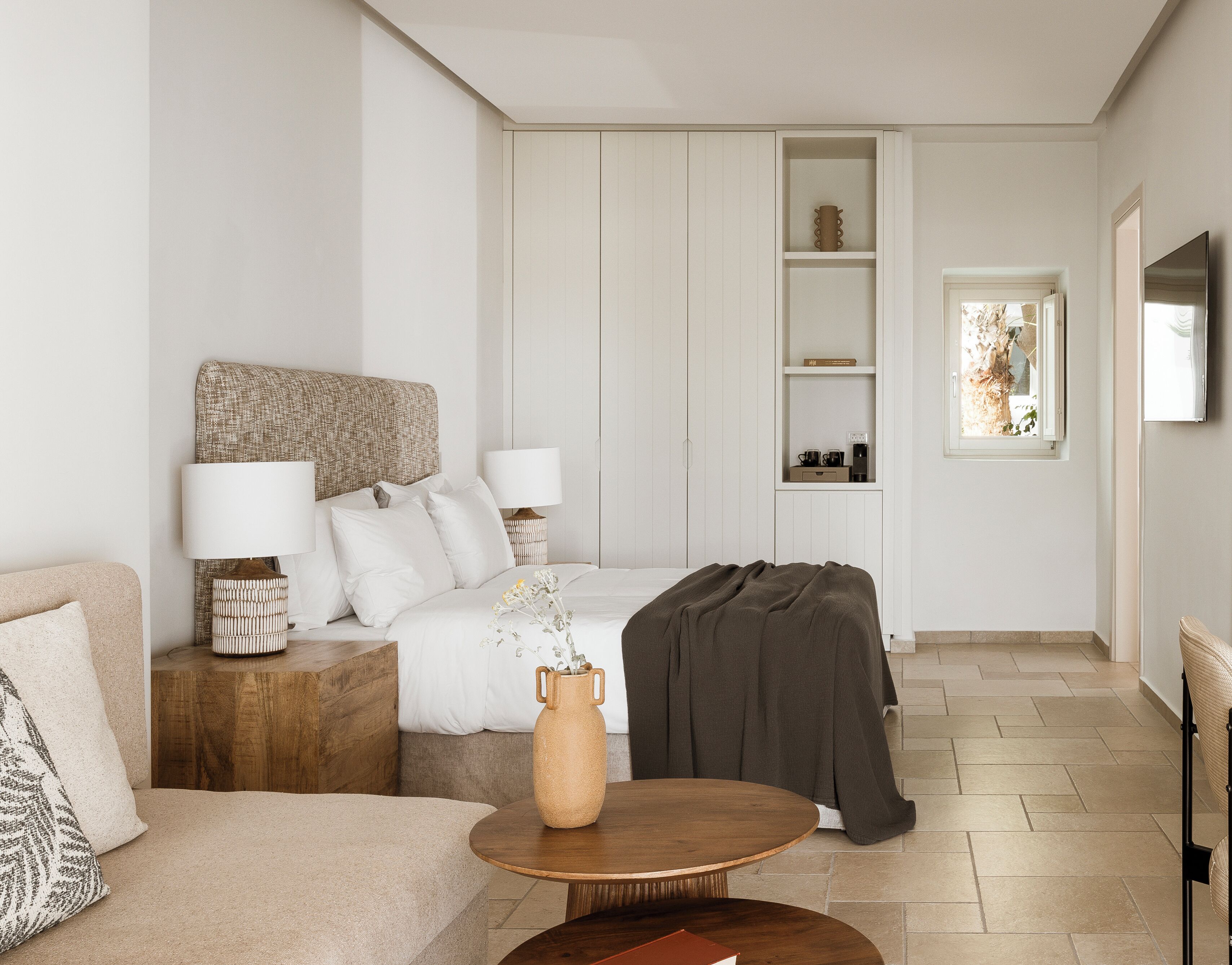 A modern hotel room with a bed, bedside tables, a sofa, a coffee table, and a TV.