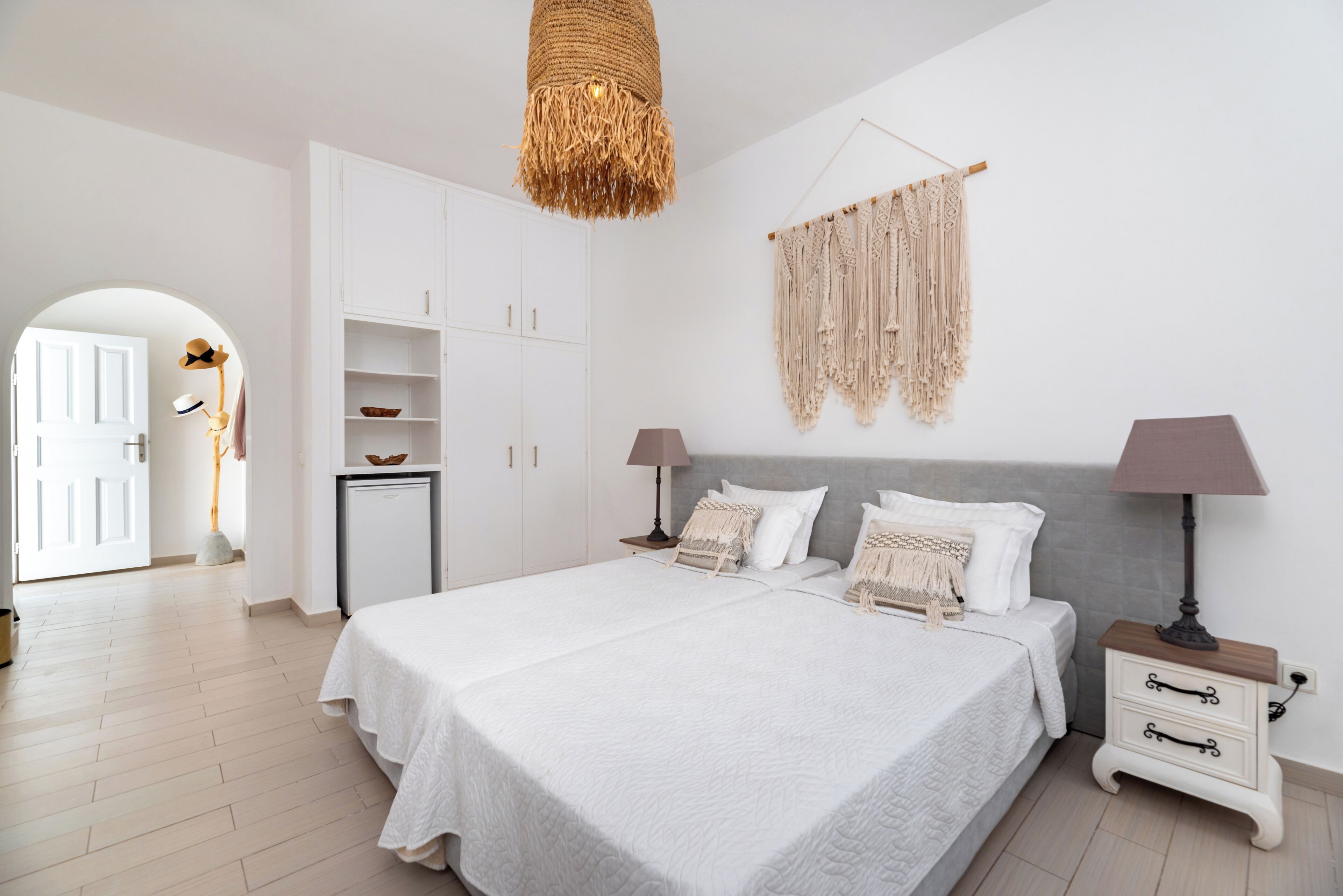 A bedroom with a double bed, bedside tables, a wardrobe, a macrame wall hanging, and a hanging light fixture.