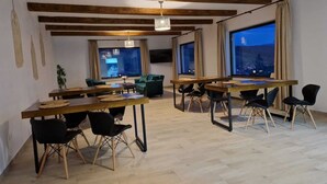 Een ruime eetruimte met houten tafels en stoelen, grote ramen met gordijnen, en een uitzicht op de stad bij zonsondergang.