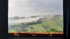 Een uitzicht op een landelijk landschap met glooiende heuvels, een nevelachtige sfeer en verspreide huizen.