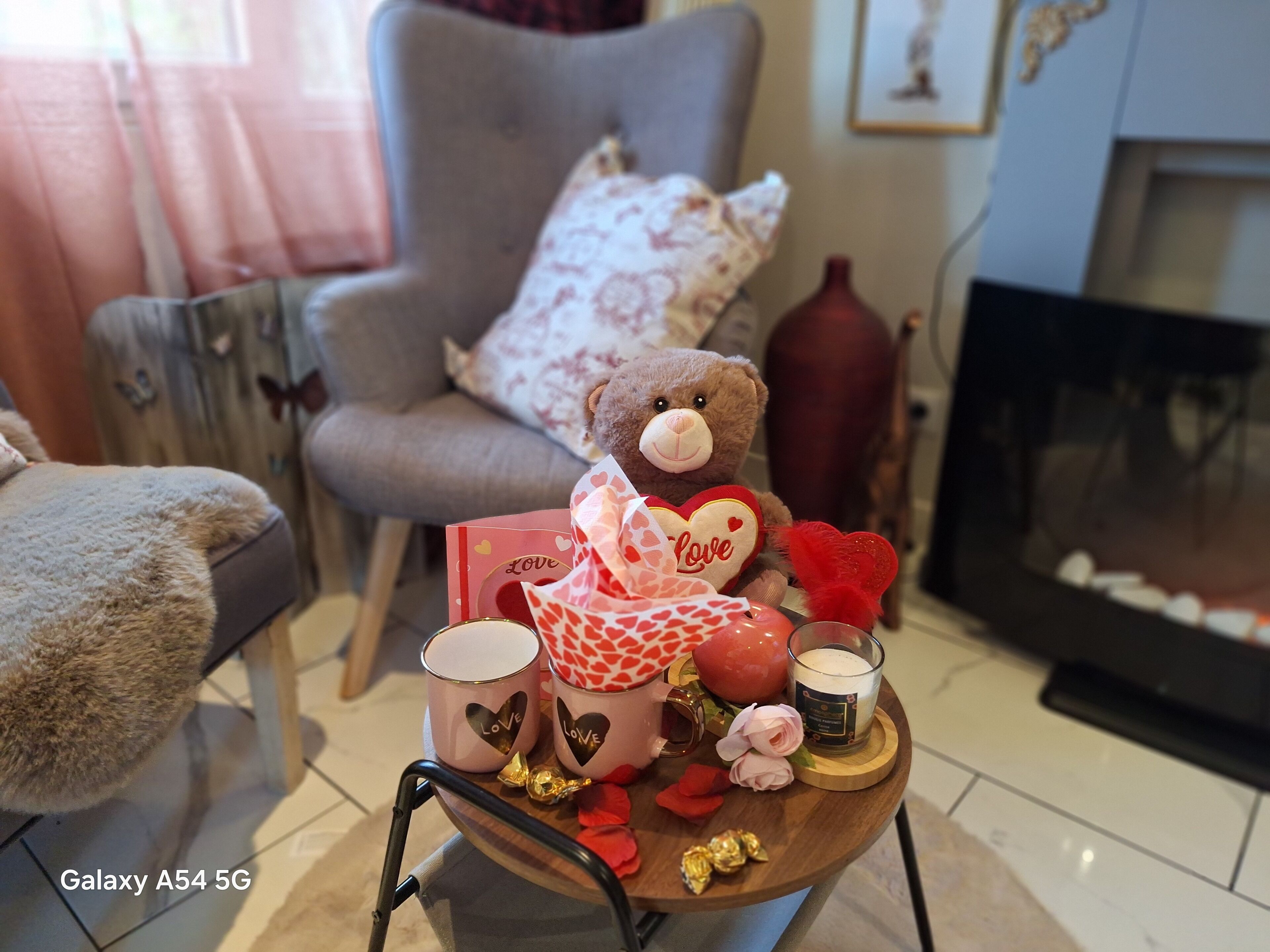 A cozy living room with a plush armchair, a teddy bear, a small table with a candle, and a fireplace.
