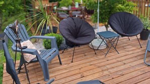 Een houten terras met buitenmeubilair, waaronder lounge stoelen, een tafeltje en een blauwe parasol.