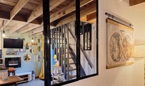 A room with a wooden ceiling, a mounted television, a world map, and a staircase with a metal railing.