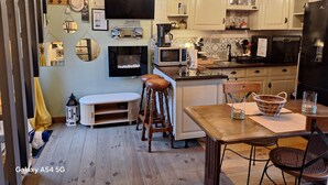 Een gezellige keuken met houten kastjes, een eettafel, krukken en een televisie aan de muur.