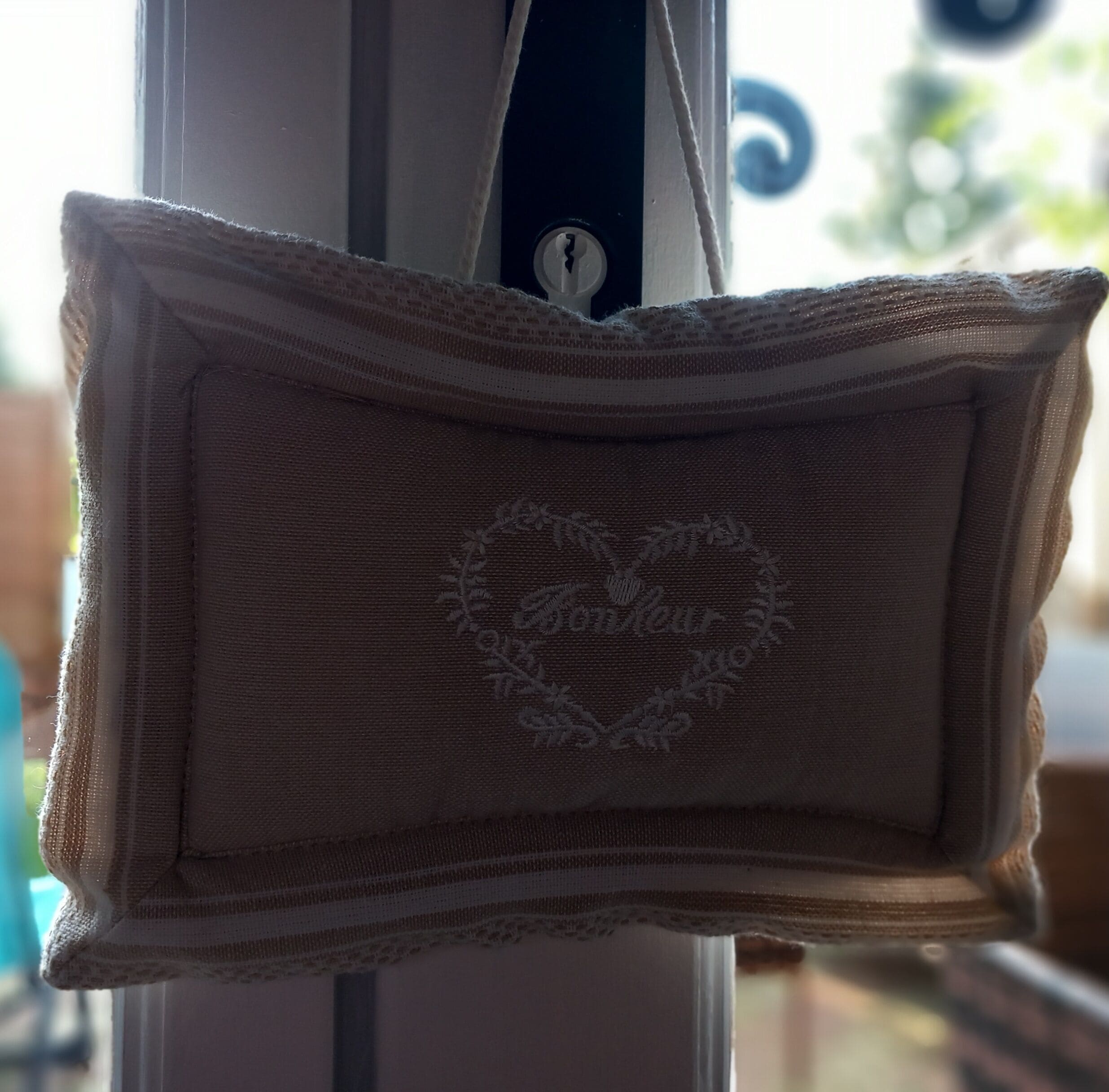 Un coussin beige orné d’une broderie florale, suspendu à une fenêtre.