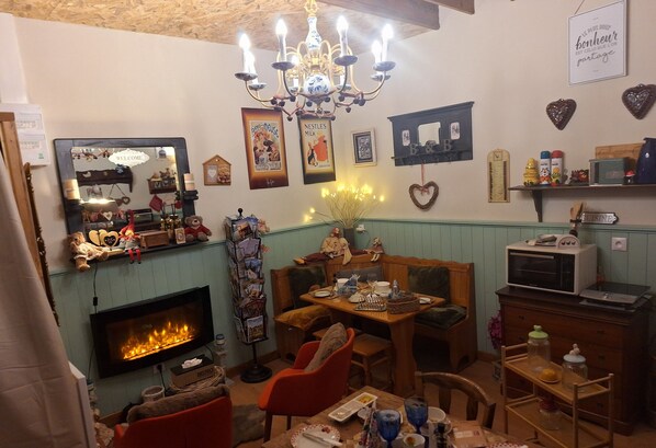 A cozy room with a fireplace, wooden furniture, and various decorations including a chandelier, framed pictures, and heart-shaped ornaments.