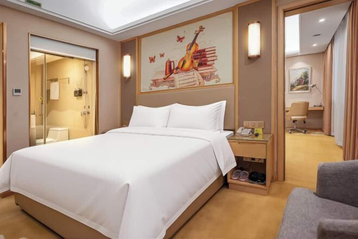 A hotel room with a large bed, a desk with a lamp, a chair, and a painting on the wall.