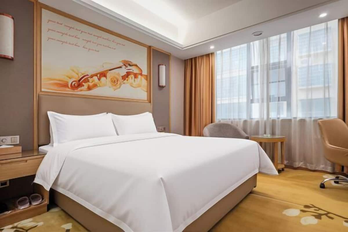 A hotel room with a large bed, a desk, a chair, and a window with curtains.