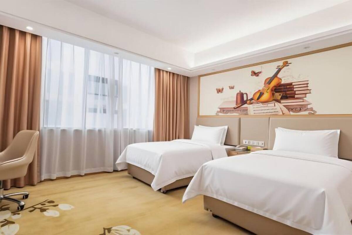 A hotel room with two beds, a chair, and a large window with curtains.