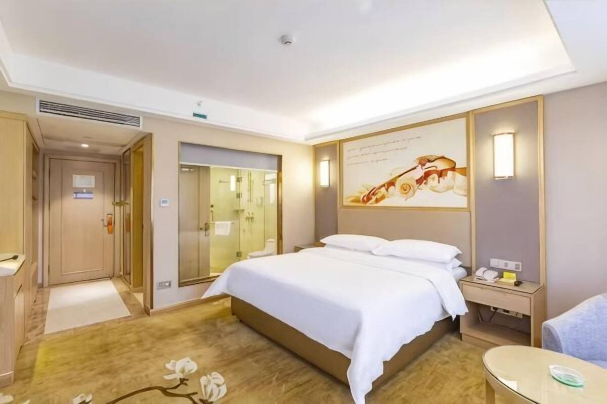 A hotel room with a bed, bedside table, lamp, and a mirror.