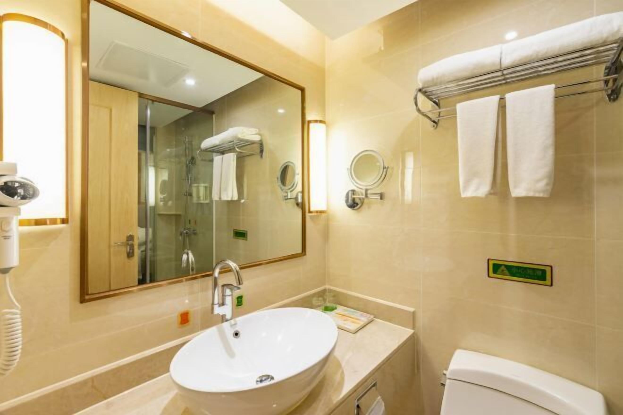 Une salle de bain avec un grand miroir, un lavabo, des toilettes et un porte-serviettes.