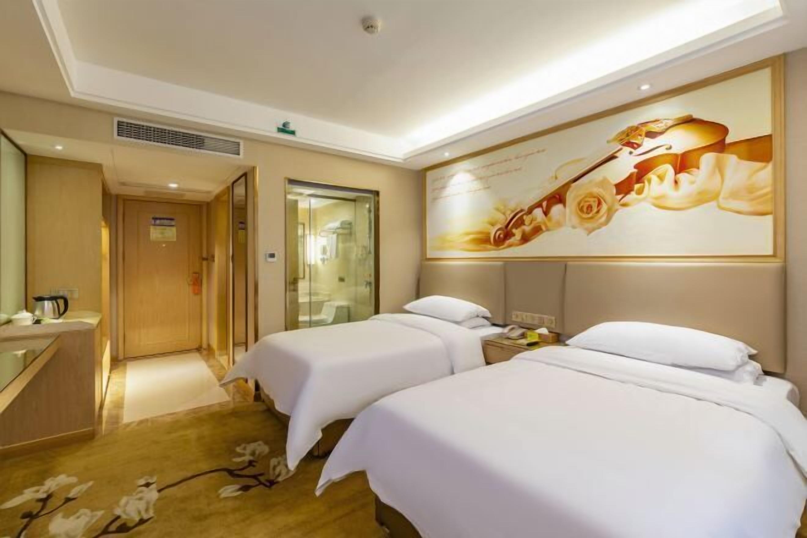 A hotel room with two beds, a large mirror, a painting, and a small desk with a telephone.