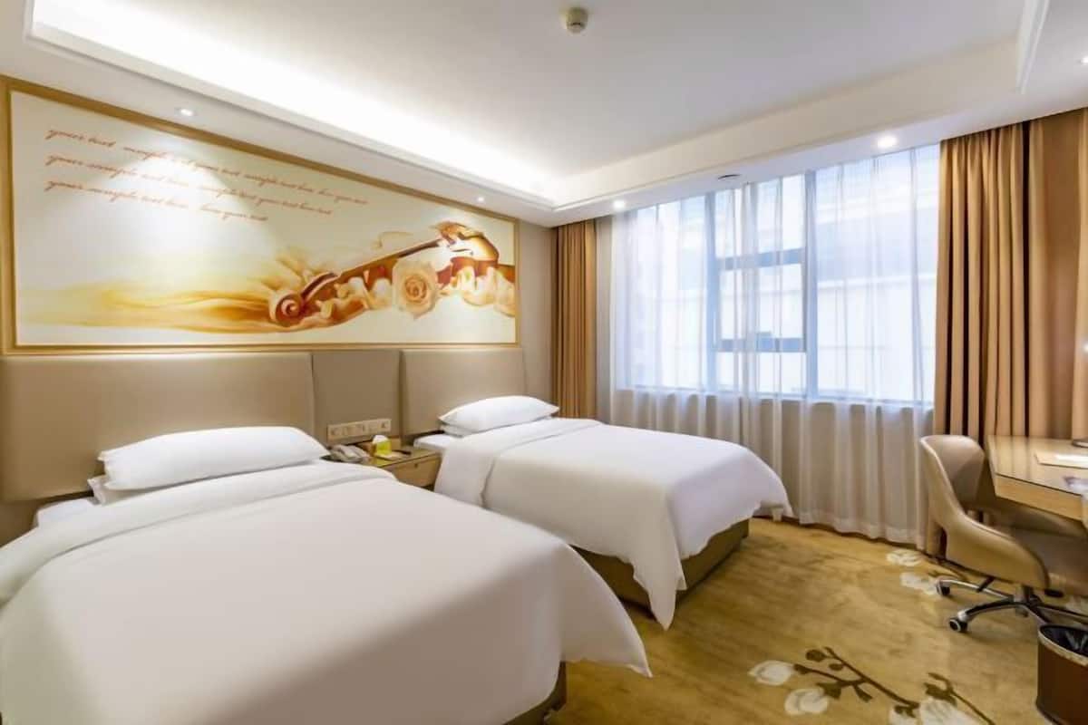 A hotel room with two beds, a desk, a chair, and a large window with curtains.