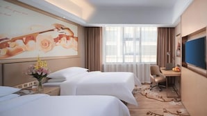 Ein Hotelzimmer mit zwei Betten, einem Schreibtisch, einem Fernseher und einem großen Fenster mit Vorhängen.
