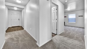 A hallway with white walls, a carpeted floor, and a door leading to another room. - Monochrome Home Near Hospital (Nampa)