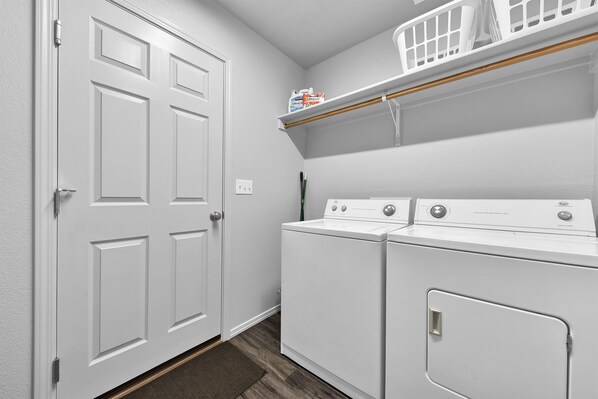 A laundry room with two stacked front-loading washers and dryers, a white door, and a shelf above the dryers.