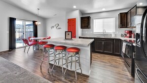 A modern kitchen with a central island, bar stools, and a red door. - Monochrome Home Near Hospital (Nampa)