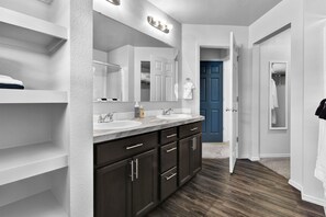 Un bagno moderno con mobili in legno scuro, ripiani bianchi e una porta blu sullo sfondo.