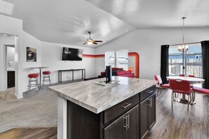 A modern kitchen with a marble island, dark cabinets, and a dining area with red chairs.